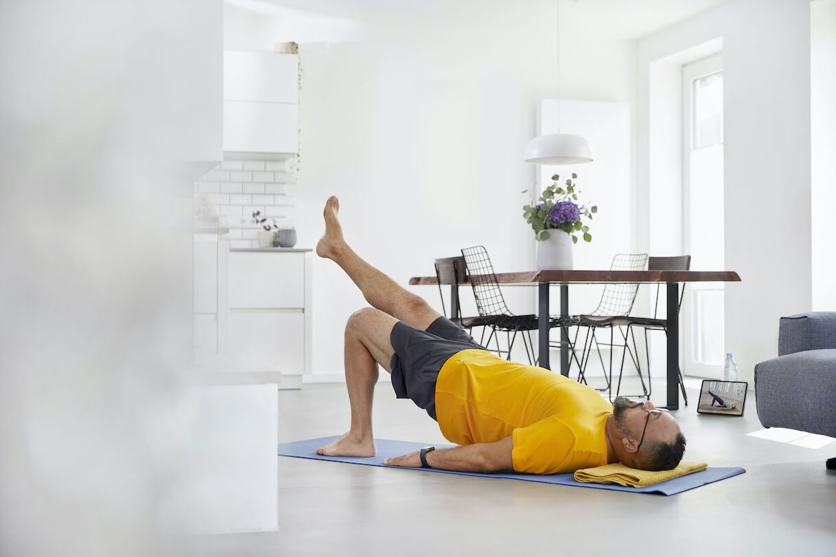 A man follows an exercise routine on his living room floor using a tablet.