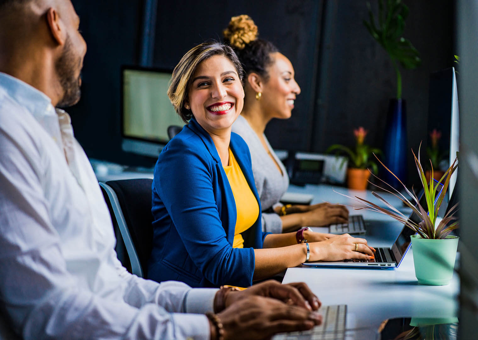 A woman sits at her laptop and smiles at her coworker.